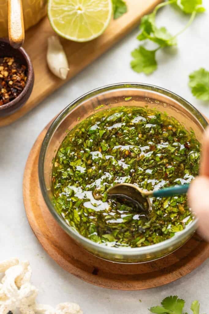 A hand stirring a bowl of homemade cilantro chimichurri