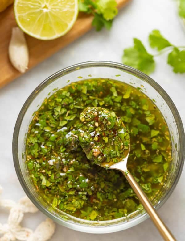 A spoon over a bowl of cilantro chimichurri with a spoonful of sauce.