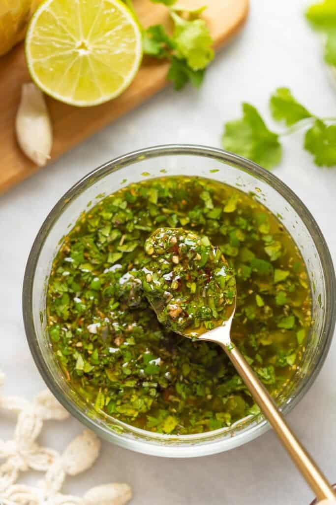 A spoon over a bowl of cilantro chimichurri with a spoonful of sauce.