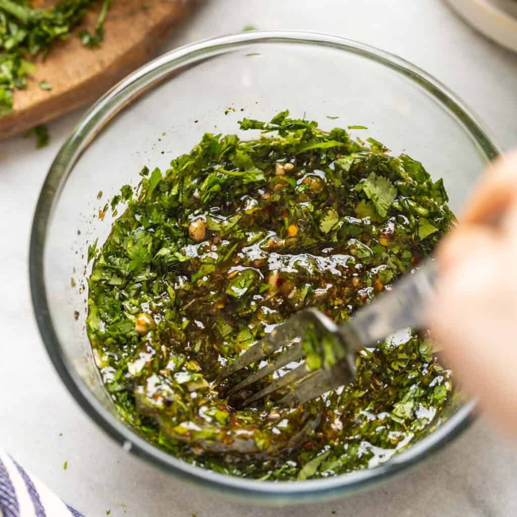 Homemade chimichurri sauce mixing together in a small bowl.