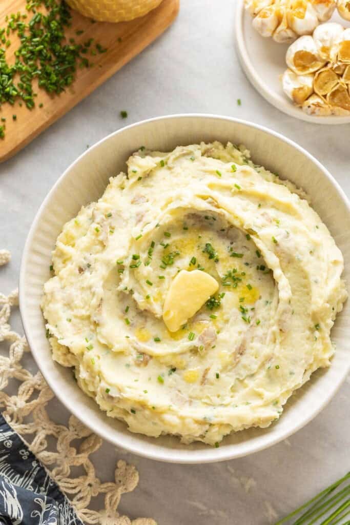 Roasted Garlic Mashed Potatoes in a serving bowl with melted butter and chopped chives on top.