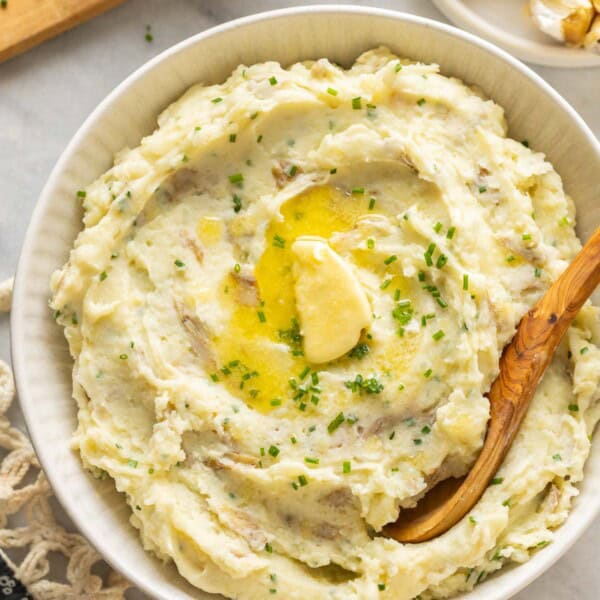 Roasted Garlic Mashed Potatoes in a serving bowl with melted butter and chopped chives on top and a serving spoon in the bowl.