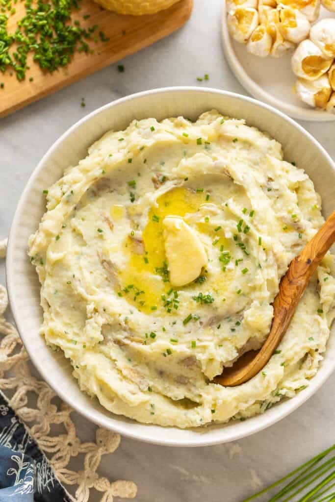 Roasted Garlic Mashed Potatoes in a serving bowl with melted butter and chopped chives on top