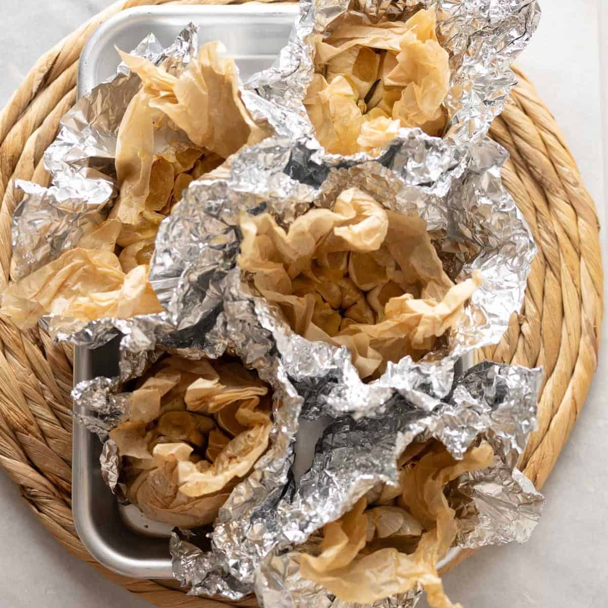 roasted garlic in foil and baking paper parcels on a baking sheet