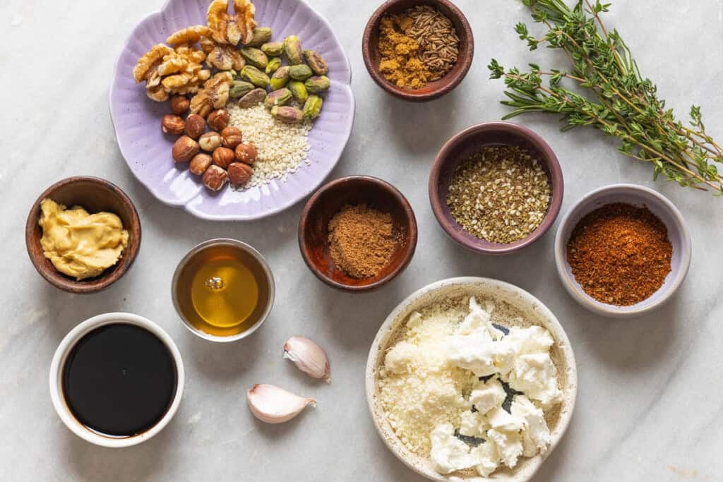 Little bowls of different ingredients that can be used to season roasted carrots: mustard, balsamic vinegar, honey, garlic, fresh herbs, nuts & seeds, cheese, za'atar and various ground spices