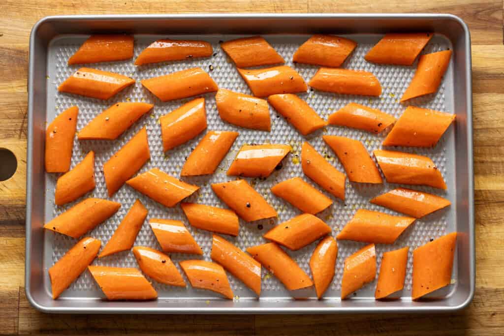 Raw carrots coated in oil and spice on a baking sheet.