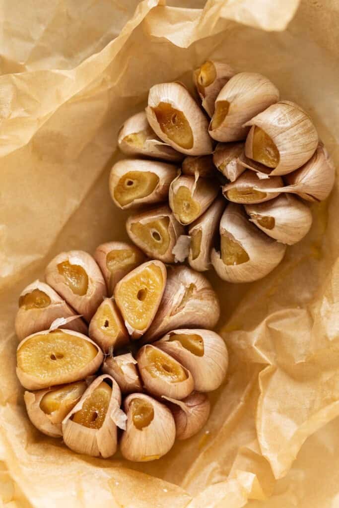 Two heads of oven roasted garlic heads in parchment paper