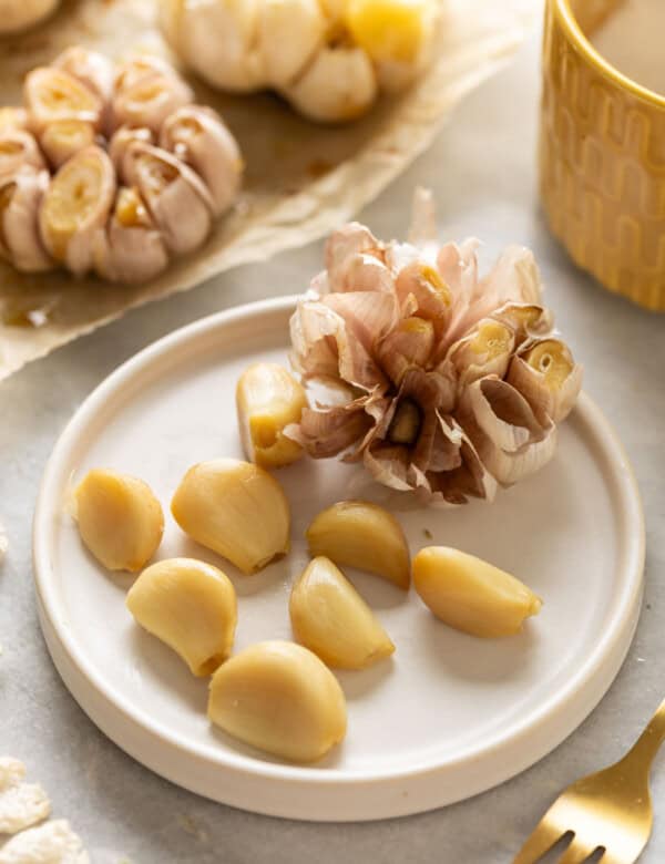 A full head of roasted garlic with some of the cloves removed from the head on a small plate.