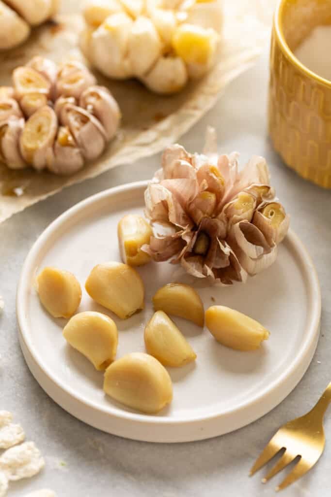 A full head of roasted garlic with some of the cloves removed from the head on a small plate.