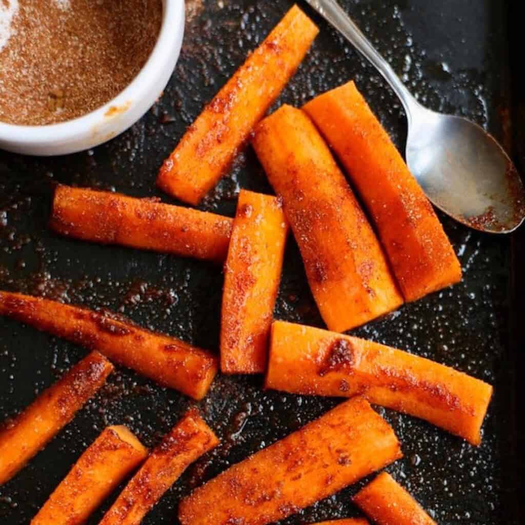 Carrot sticks on a baking sheet tossed in oil and spice