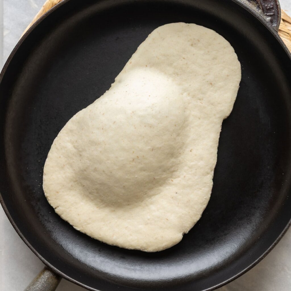 gluten free naan dough cooking on a hot cast iron pan - a large air pocket puffing up as it cooks