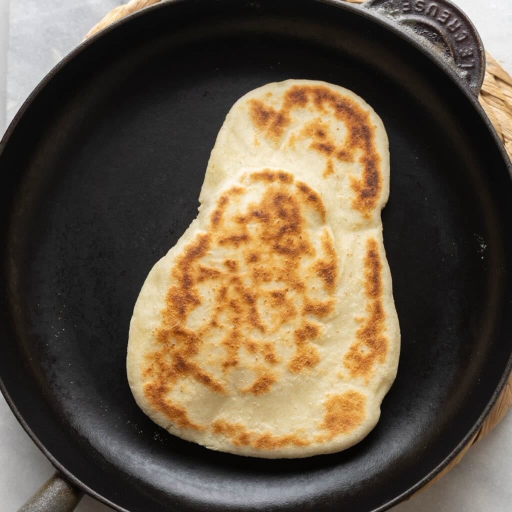 gluten free naan in a cast iron pan - the top is golden brown & lightly blistered