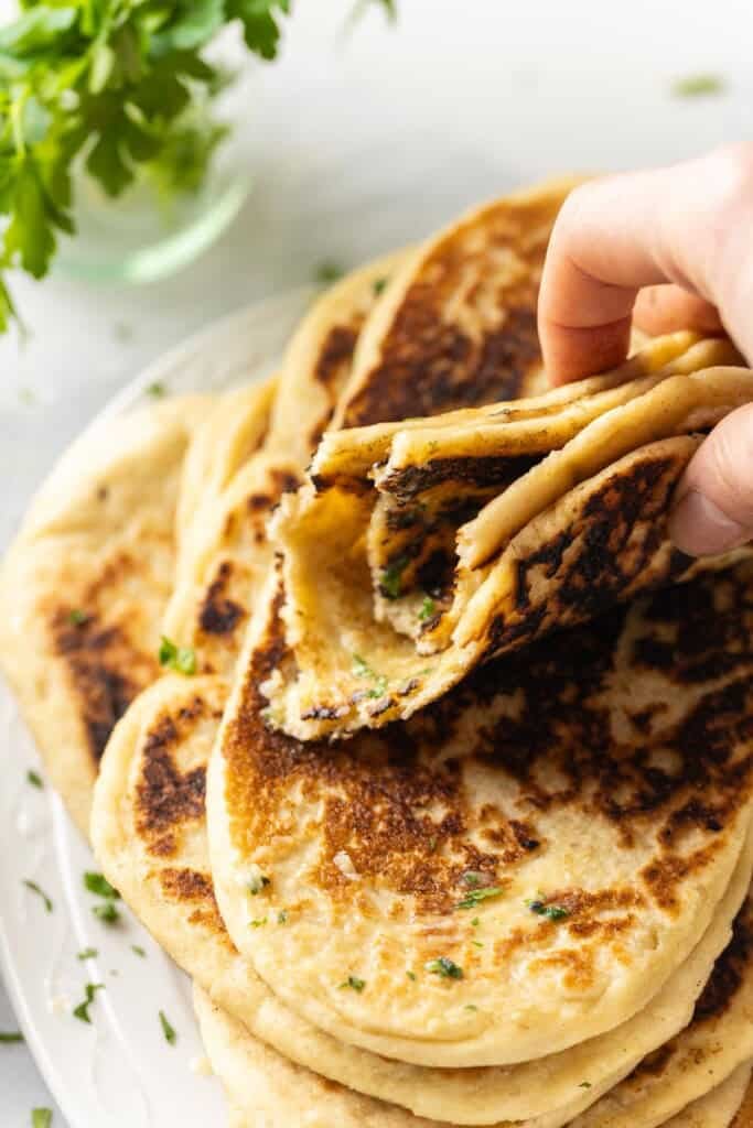 A hand holding up a gluten free naan torn in half and folded up