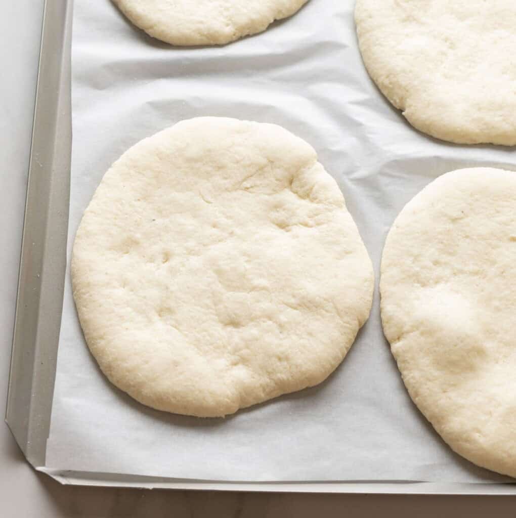gluten free pita dough slightly puffed up after rising on a baking sheet