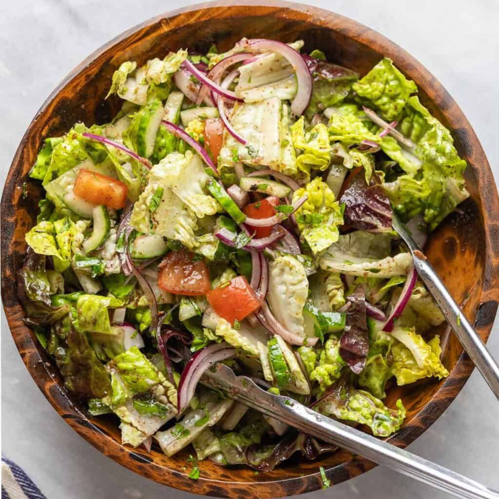 Fattoush salad with the fried pita chips in a salad bowl, tossed together with a pair of kitchen tongs