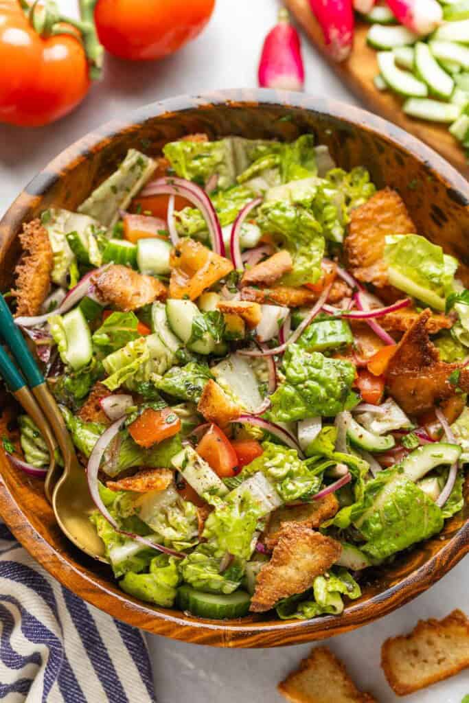 Fattoush salad with gluten free pita chips, chopped tomatoes, red onion, cucumber, radishes, mint, parsley, romaine lettuce in a large salad bowl.