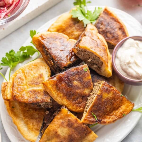 A platter full of gluten free arayes (Lebanese meat stuffed pitas) wedges and a small bowl of tahini yoghurt sauce