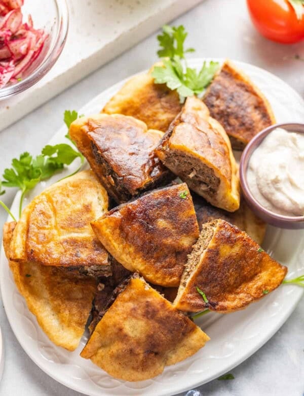 A platter full of gluten free arayes (Lebanese meat stuffed pitas) wedges and a small bowl of tahini yoghurt sauce