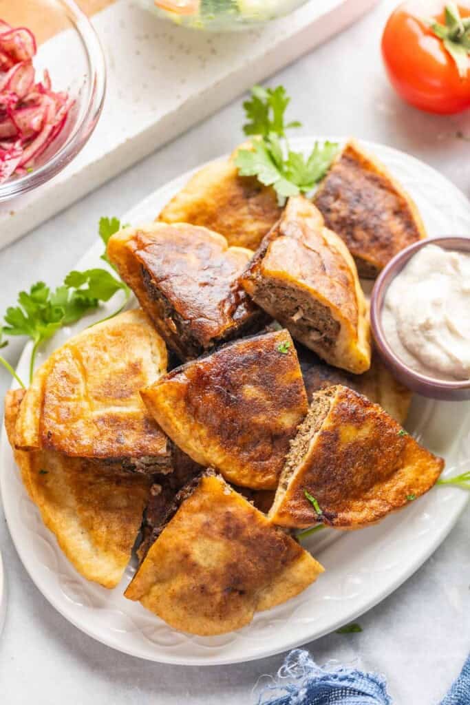 A platter full of gluten free arayes (Lebanese meat stuffed pitas) wedges and a small bowl of tahini yoghurt sauce
