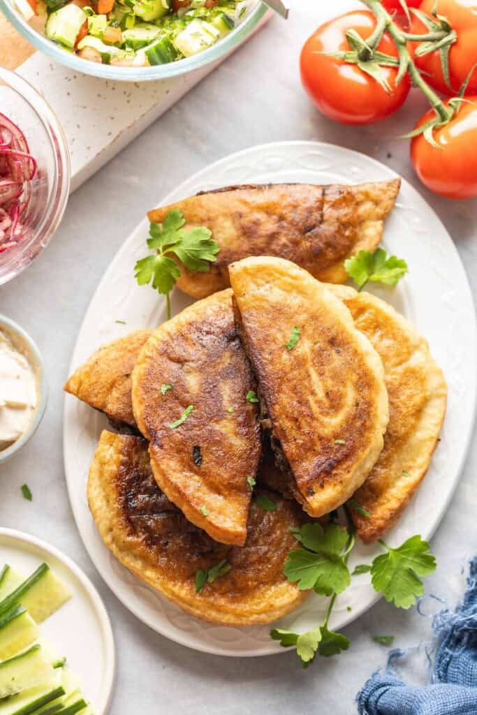 A platter full of gluten free arayes (Lebanese meat stuffed pitas) surrounded by fresh herbs, cucumber, onions and tomatoes