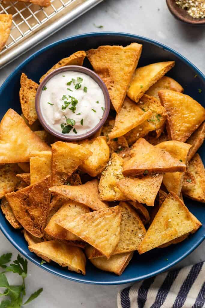 A bowl full of homemade baked gluten free pita chips with za'atar spice and a yogurt tahini dipping sauce