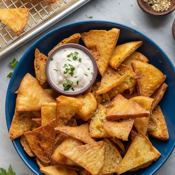 A bowl full of homemade gluten free pita chips (baked & fried) with a yogurt tahini dipping sauce