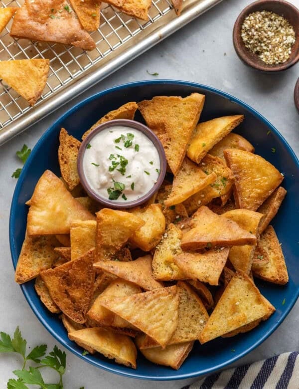 A bowl full of homemade gluten free pita chips (baked & fried) with a yogurt tahini dipping sauce