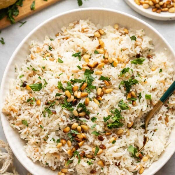 Lebanese rice made with gluten free noodles, toasted pine nuts and fresh chopped parsley in a serving dish with a spoon