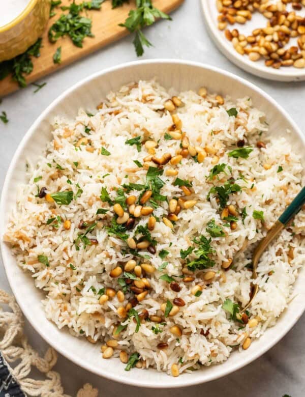 Lebanese rice made with gluten free noodles, toasted pine nuts and fresh chopped parsley in a serving dish with a spoon