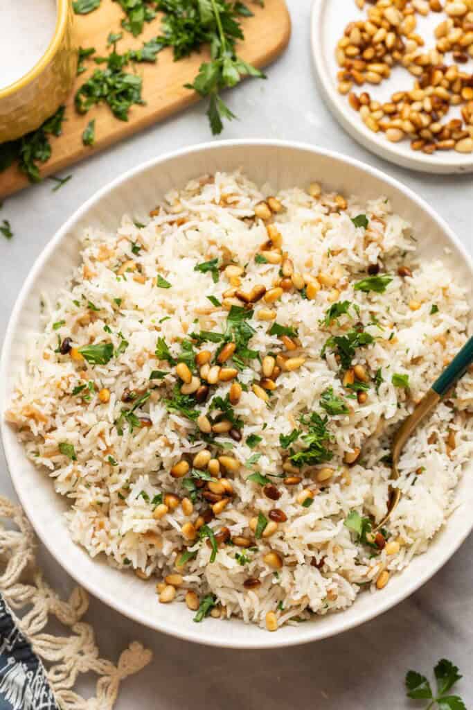 Lebanese rice made with gluten free noodles, toasted pine nuts and fresh chopped parsley in a serving dish with a spoon