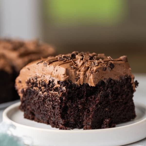 A slice of gluten free chocolate zucchini cake with chocolate buttercream frosting on a plate with a bite taken out