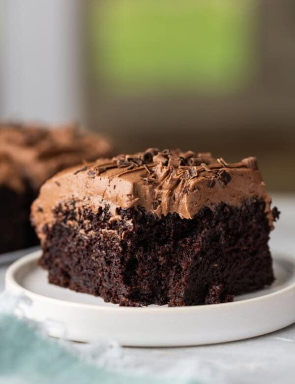 A slice of gluten free chocolate zucchini cake with chocolate buttercream frosting on a plate with a bite taken out