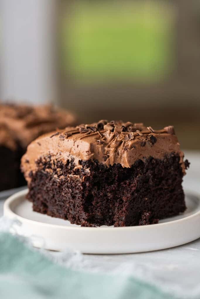 A slice of gluten free chocolate zucchini cake with chocolate buttercream frosting on a plate with a bite taken out