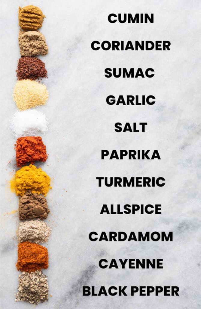 1/4 tsp of individual spices in a homemade shawarma spice blend in a row. From top to bottom: cumin, coriander, sumac, garlic, salt, paprika, turmeric, allspice, cardamom, cayenne, black pepper