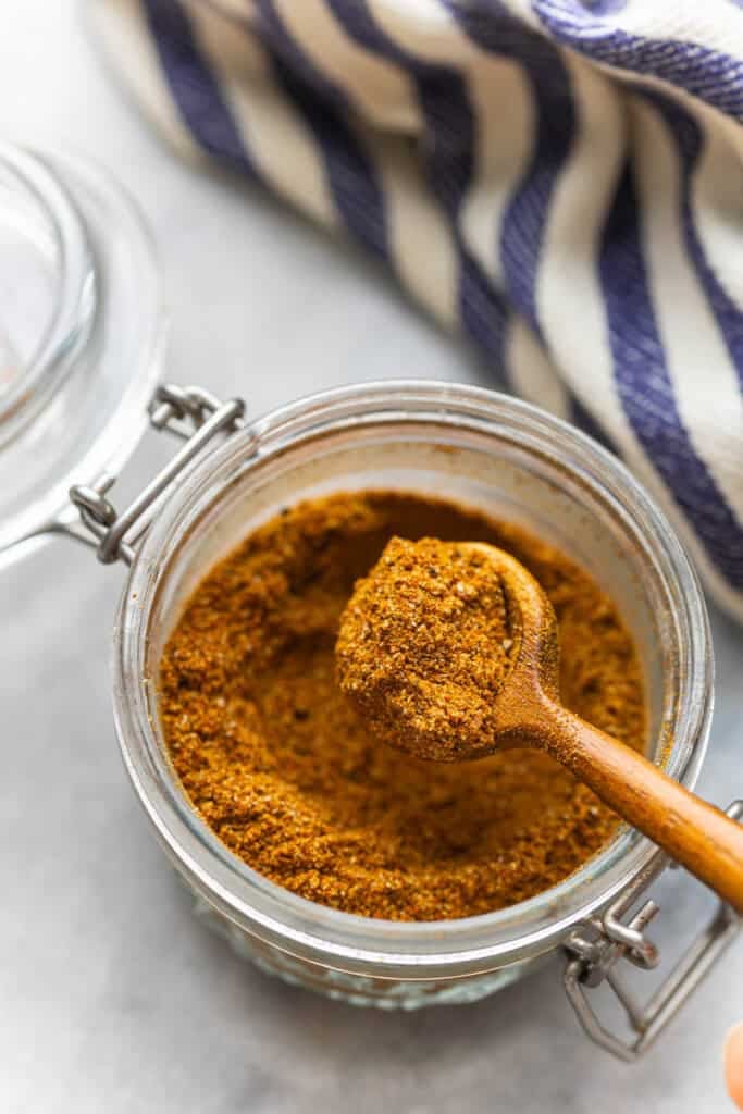 A wooden spoon full of a homemade shawarma spice blend over a small jar.