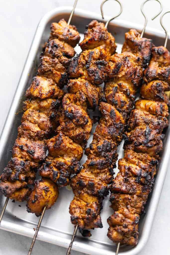 Shawarma chicken kebab skewers resting on a baking sheet.
