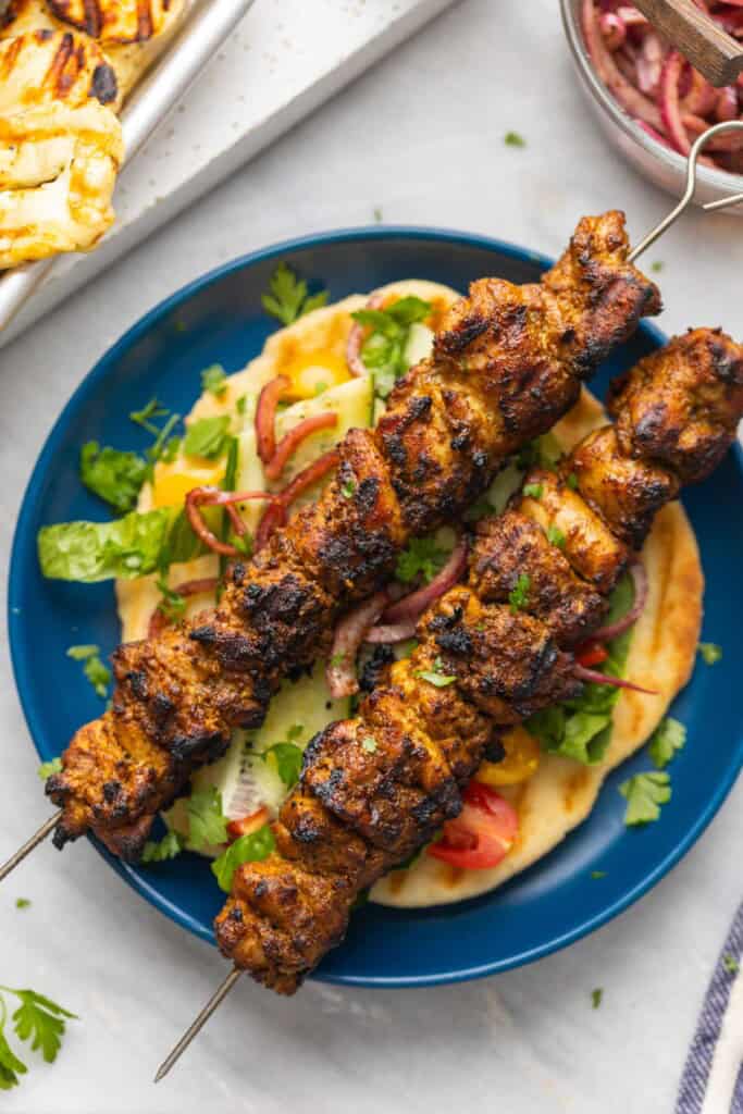 Two shawarma chicken skewers over a gluten free pita with salad.