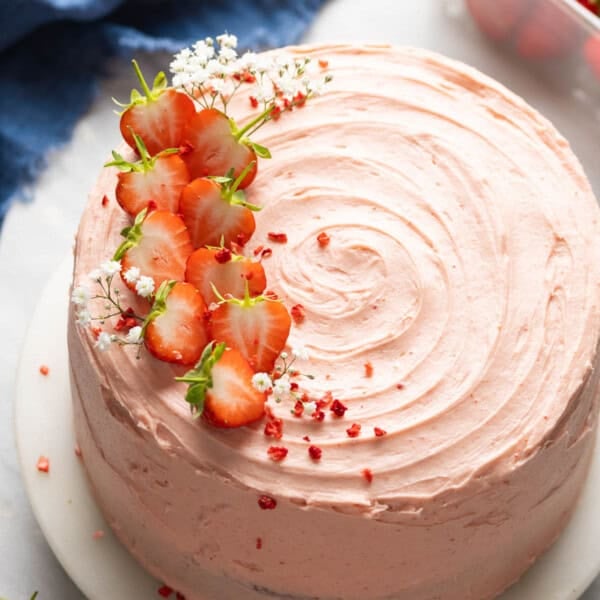 Gluten free strawberry cake frosted with a strawberry buttercream and decorated with fresh strawberries and baby's breath flowers on a top sitting on a cake stand.