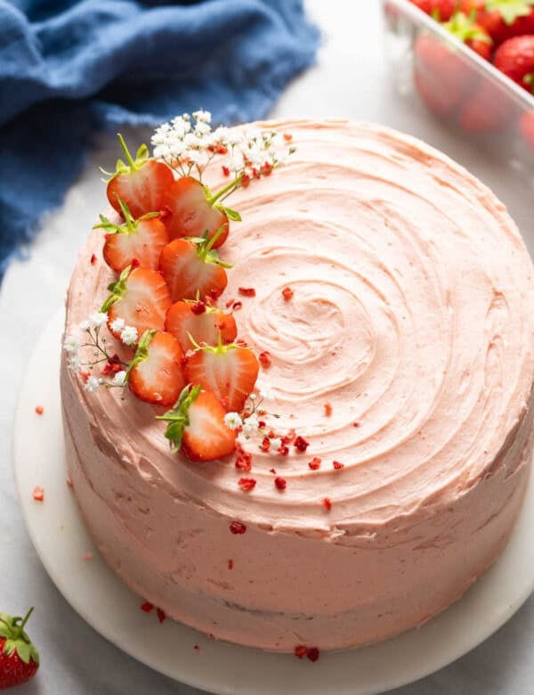 Gluten free strawberry cake frosted with a strawberry buttercream and decorated with fresh strawberries and baby's breath flowers on a top sitting on a cake stand.