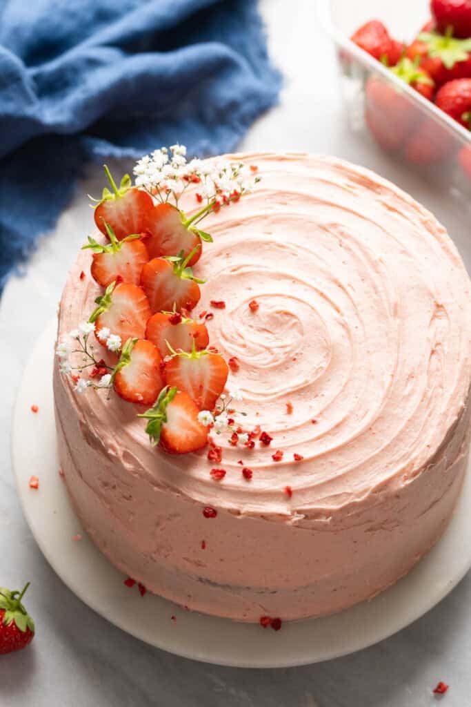 Gluten free strawberry cake frosted with a strawberry buttercream and decorated with fresh strawberries and baby's breath flowers on a top sitting on a cake stand.