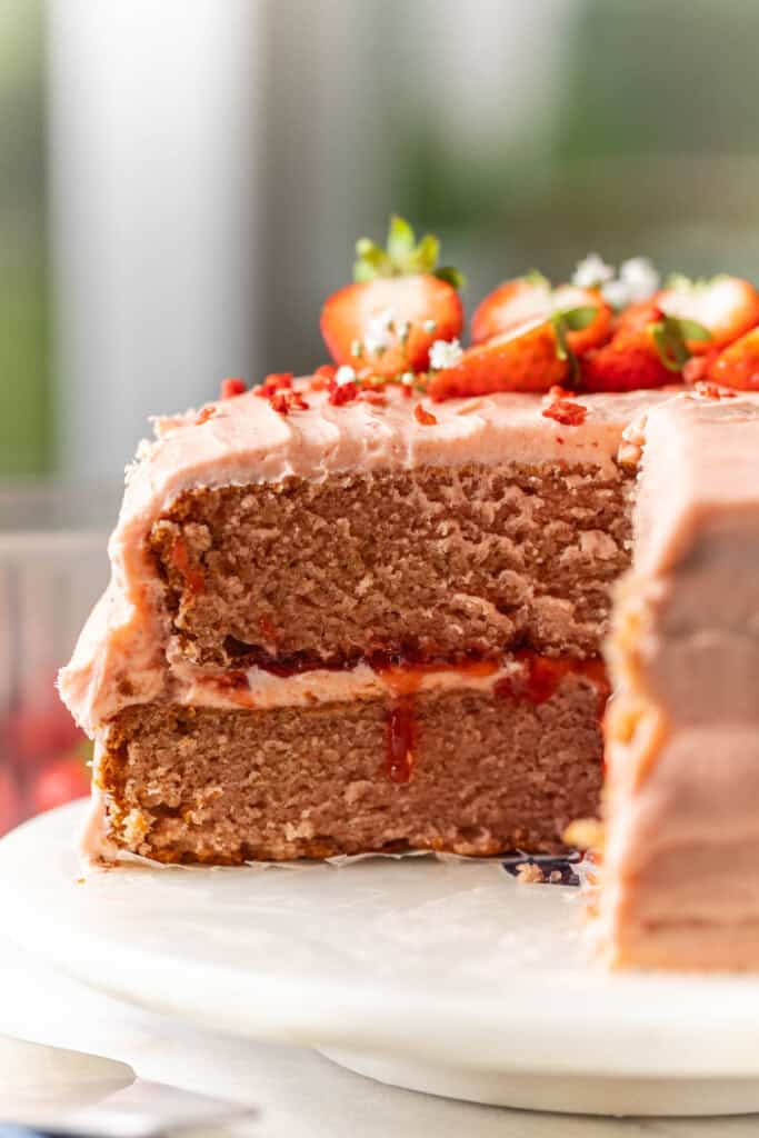 A slice taken from a gluten free strawberry cake to show the inside of the two layer cake filled with strawberry jam and buttercream frosting