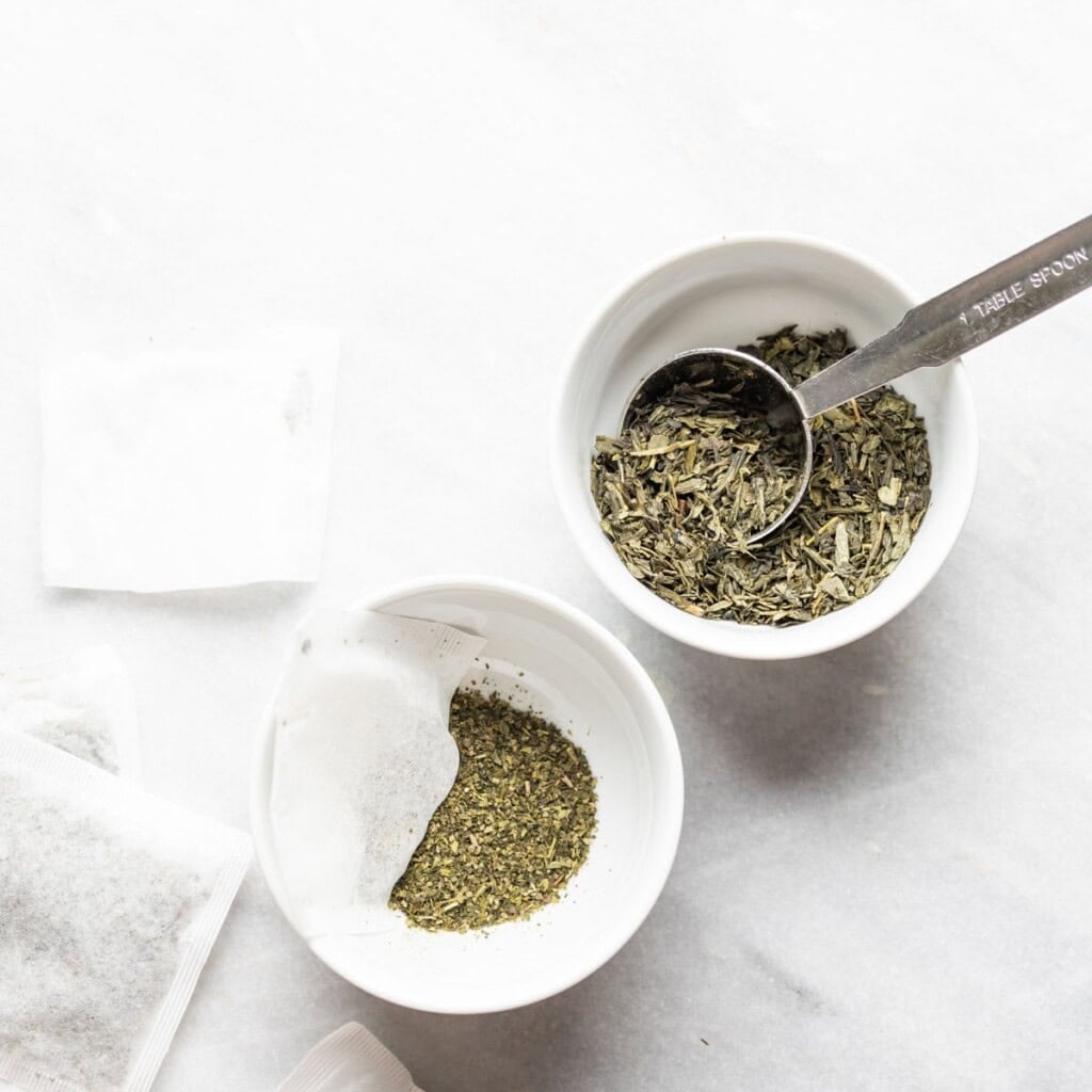 Loose leaf green tea leaves and tea leaves from a bag in two little bowls.