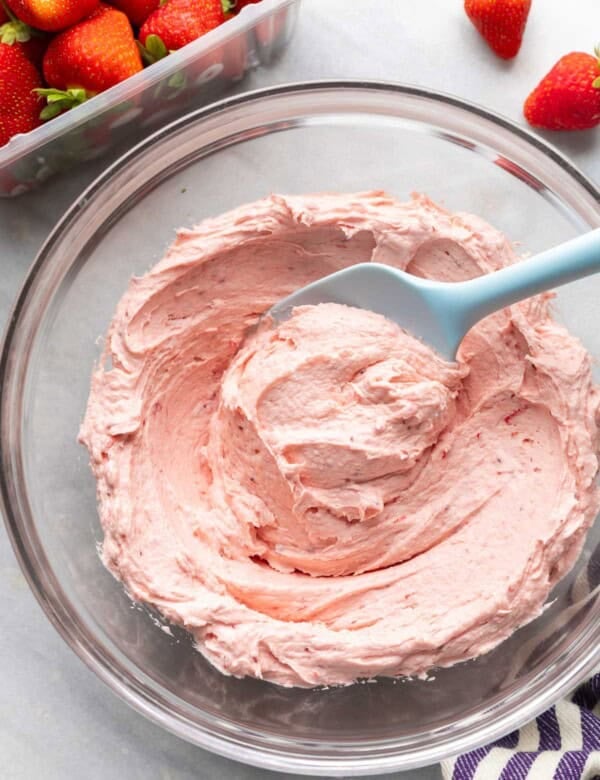 homemade strawberry buttercream in a mixing bowl with a rubber spatula and fresh strawberries on the side