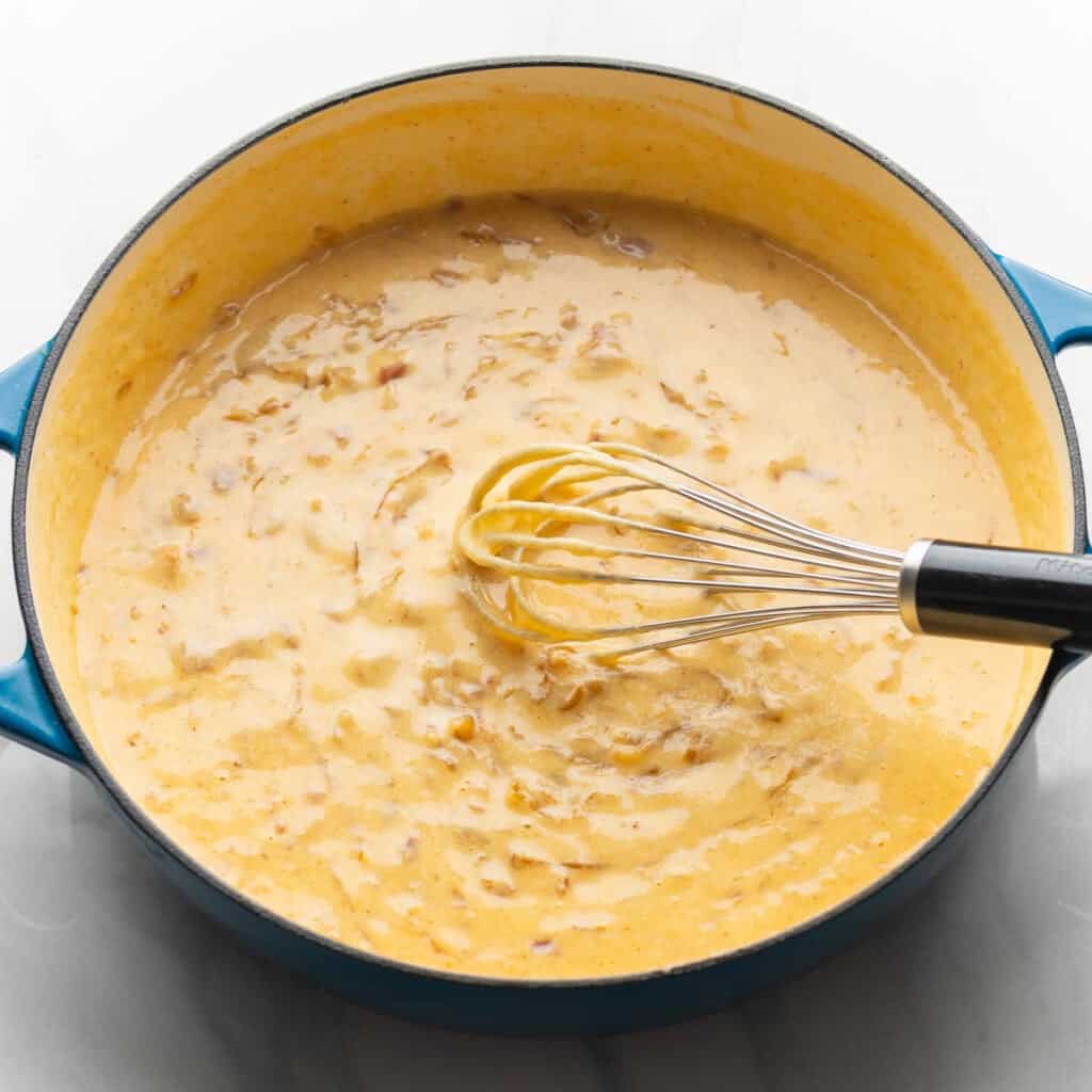 caramelized onion, bacon & cider cheese sauce in a casserole dish with a whisk