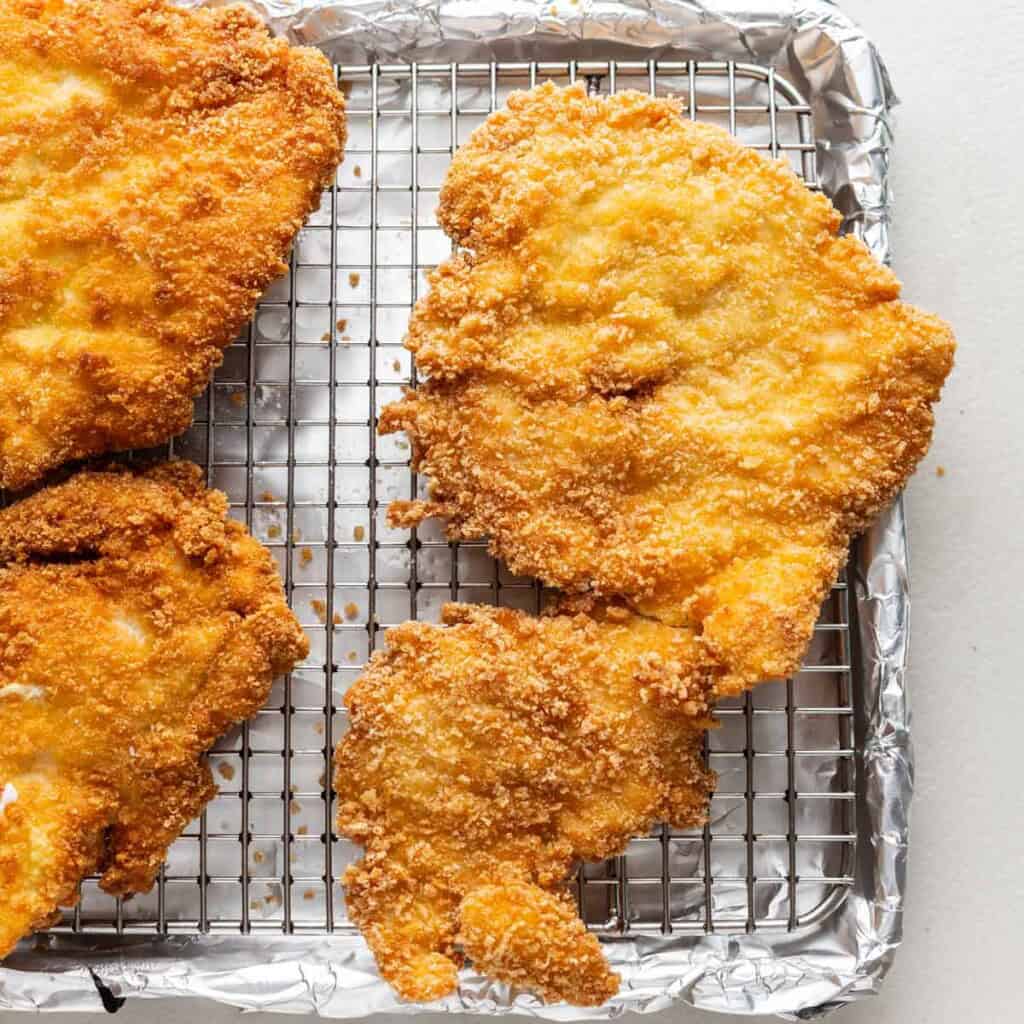 gluten free schnitzel resting on a wire cooling rack over a baking sheet lined with foil