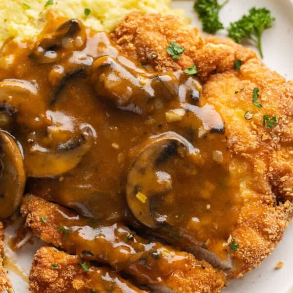 Gluten free schnitzel covered with a mushroom gravy and fresh, chopped parsley with a side of mashed potatoes and a lemon wedge.