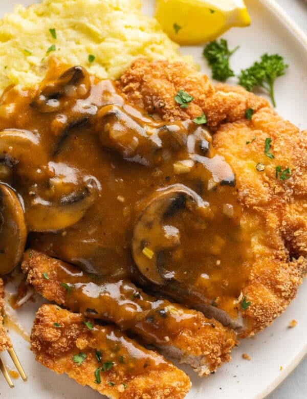 Gluten free schnitzel covered with a mushroom gravy and fresh, chopped parsley with a side of mashed potatoes and a lemon wedge.