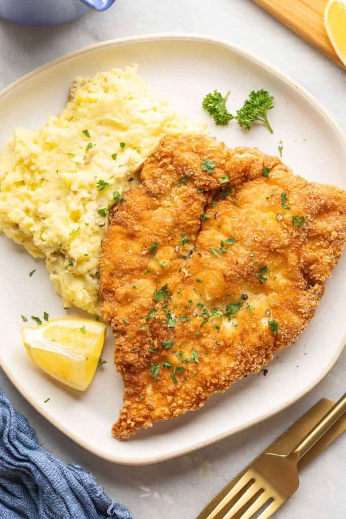 Gluten free schnitzel with chopped parsley on a plate with mashed potatoes, a lemon wedge