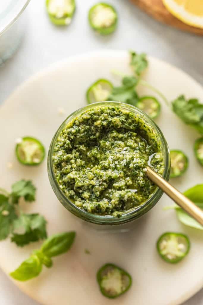 Jalapeno peso in a jar with a spoon inside and fresh basil and chili slices on the side