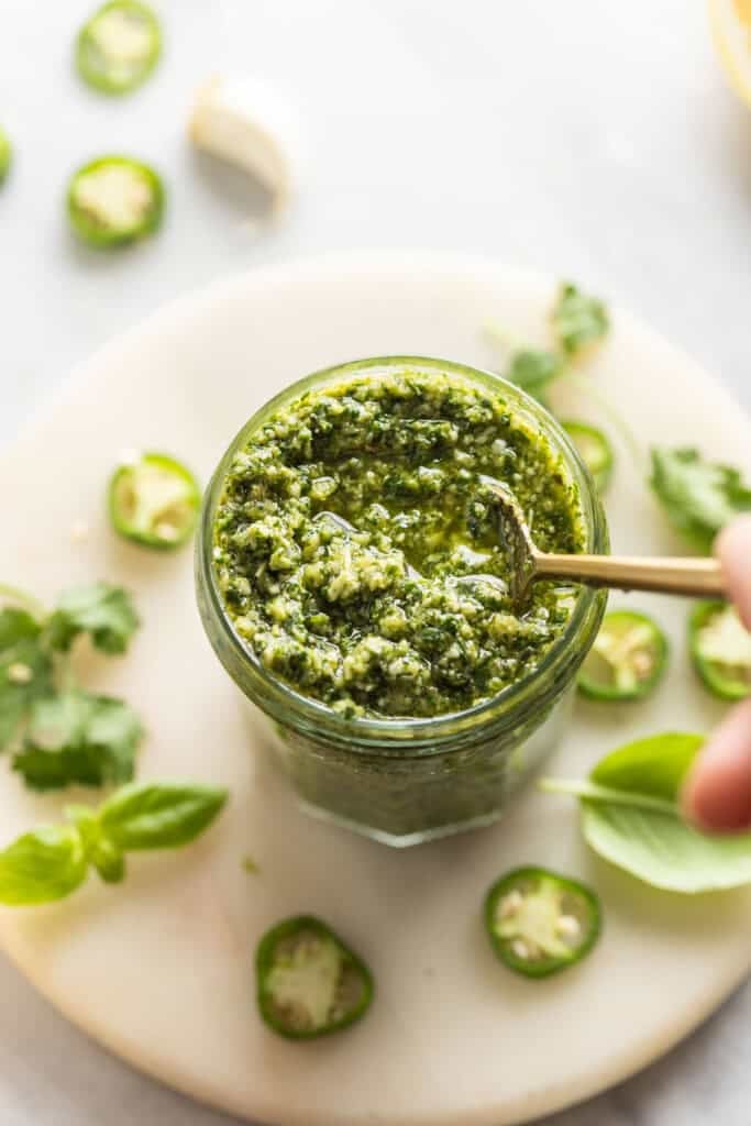 A spoon stirring a jar full of homemade jalapeno pesto